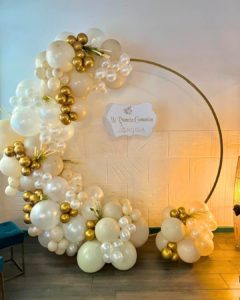 Aro dorado con globos blancos y dorados cubriendo la mitad del aro y con un letrero que dice primera comunión Angela