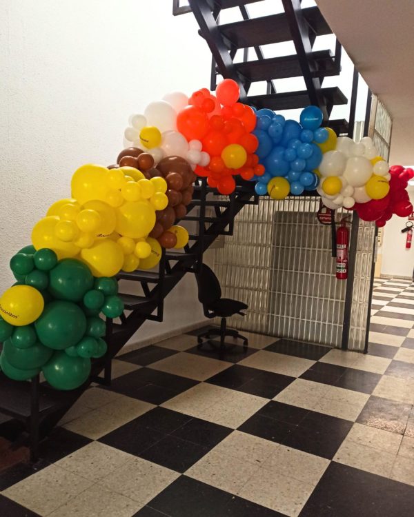 Guirnalda de globos naranja, verde, amarillo. azul y blanco a lo largo de una escalera