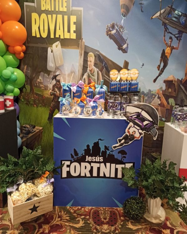 Imagen de detalle de la decoración con globos de una primera comunión, se aprecia un panel de varios metros con una imagen gigante del Juego Fortnite con varias mesas con colores a juego delante y una guirnalda de globos a un lado