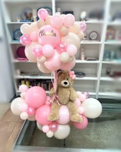 Arbol de globos rosados y blancos con un oso de peluche en el centro