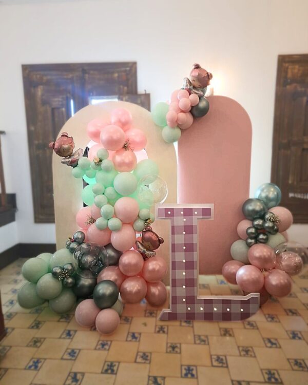 Panel en forma de arco con globos de colores pastel acompañado de otro panel rosado con mini guirnaldas de globos. y una letra L gigante de 1 metro de alto con textura y colores a juego